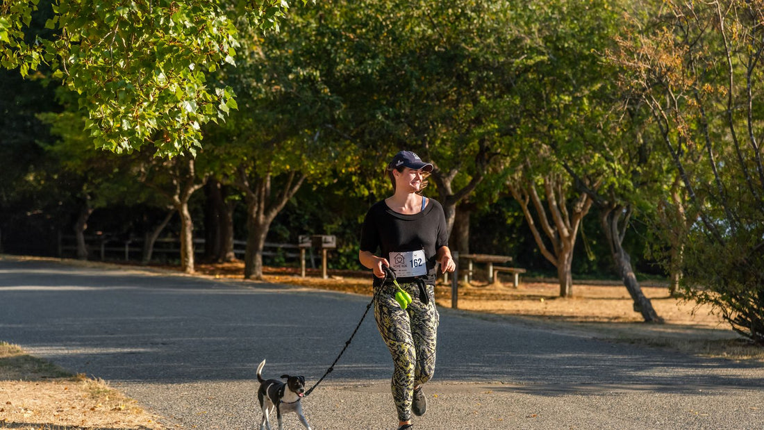 Woman running with her dog on a leash in a sunny park